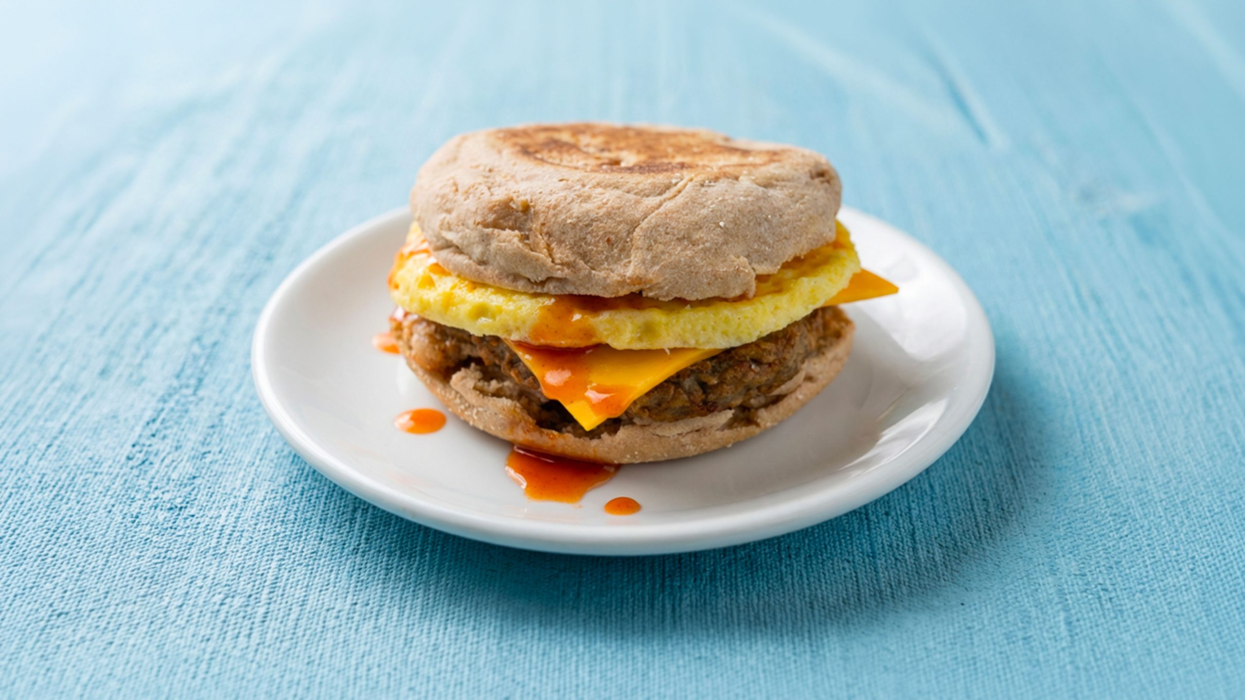 Hot honey turkey sausage breakfast sandwich with english muffin on white plate